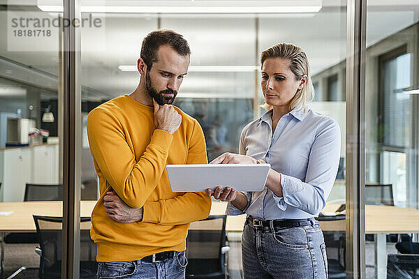 Geschäftsmann mit der Hand am Kinn blickt auf den Tablet-PC  der von einem Kollegen im Büro gehalten wird
