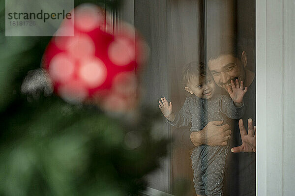 Vater und Sohn schauen aus dem Fenster auf den Weihnachtsbaum im Haus