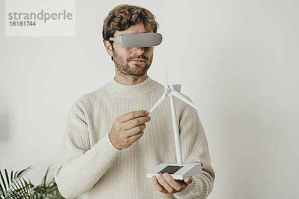 Geschäftsmann beobachtet Windturbinenmodell durch VR-Brille vor weißer Wand