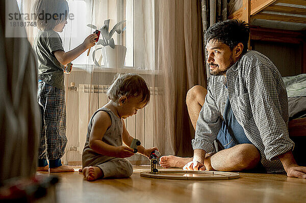 Vater sitzt auf dem Boden und seine Söhne spielen zu Hause