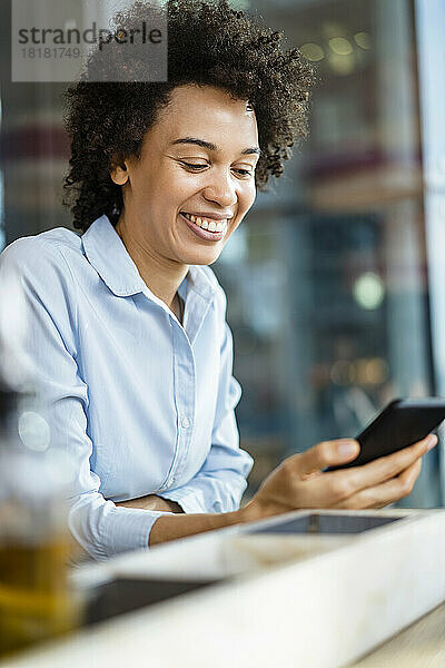 Glückliche Geschäftsfrau  die im Büro ihr Smartphone nutzt