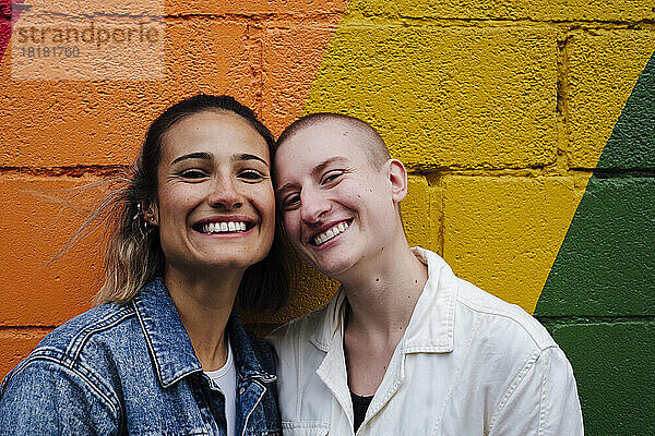 Fröhliches lesbisches Paar steht vor einer bunten Wand