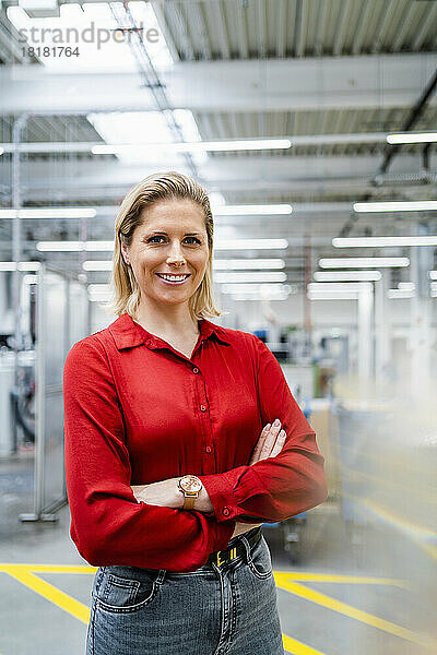 Selbstbewusste Geschäftsfrau lächelt und steht mit verschränkten Armen in der Fabrik