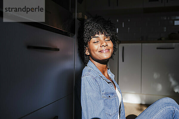 Lächelnde Frau entspannt sich und genießt das Sonnenlicht in der heimischen Küche
