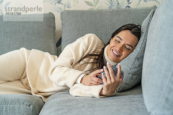 Happy young woman using smart phone on sofa at home