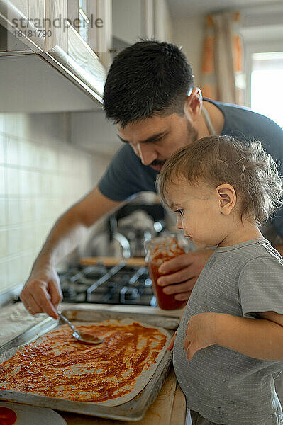 Junge und Vater verteilen in der Küche Tomatensoße auf Pizzateig