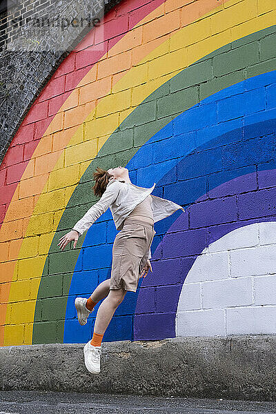 Junge Frau springt vor regenbogenfarbener Wand