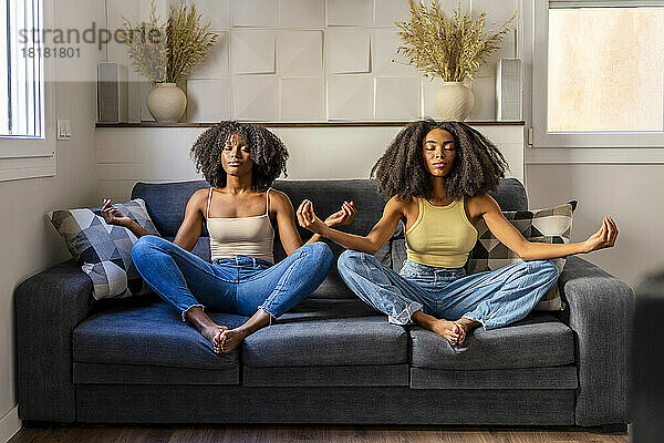 Junges lesbisches Paar meditiert auf dem Sofa im Wohnzimmer