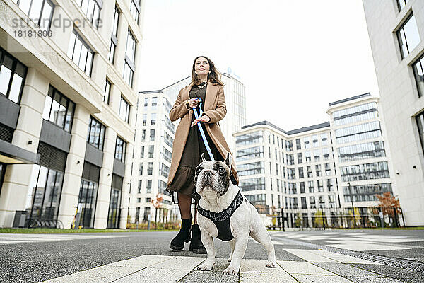 Frau läuft mit französischer Bulldogge vor Gebäuden