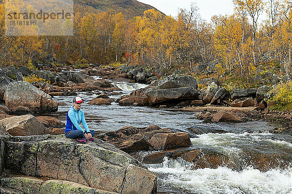 Frau sitzt auf Felsen am Flussufer