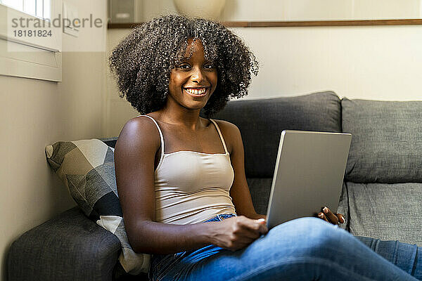 Glückliche Frau mit Laptop sitzt auf dem Sofa im Wohnzimmer