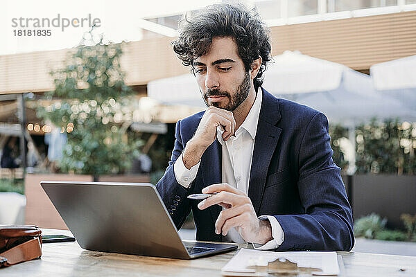Konzentrierter Geschäftsmann mit der Hand am Kinn und Blick auf den Laptop