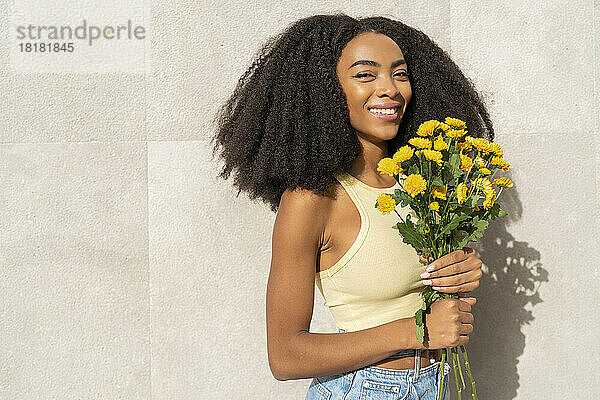 Lächelnde Frau mit gelben Blumen vor weißer Wand