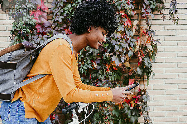 Junge Frau mit Rucksack benutzt Smartphone von Ivy Wall