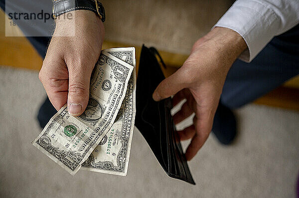 Mann hält US-Dollar-Scheine und Geldbörse