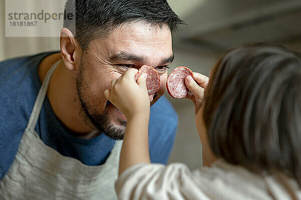 Sohn hält Peperoni über das Gesicht seines Vaters in der heimischen Küche