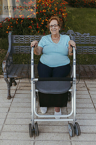Lächelnde ältere Frau vor einem Rollator  der auf einer Bank sitzt