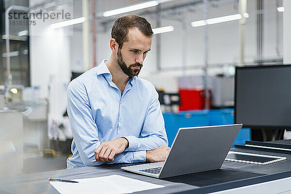 Konzentrierter Geschäftsmann beobachtet Laptop in der Fabrik