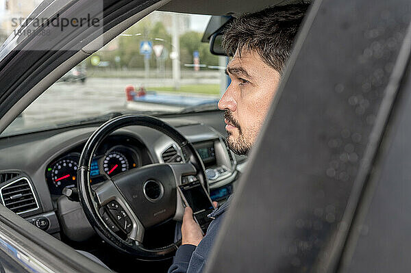 Nachdenklicher Mann mit Smartphone sitzt im Auto