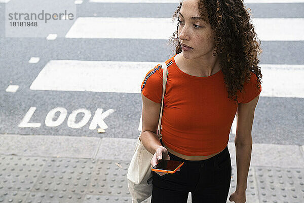 Young woman with smart phone crossing road