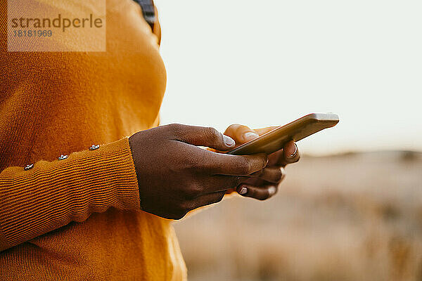 Junge Frau benutzt Mobiltelefon bei Sonnenuntergang