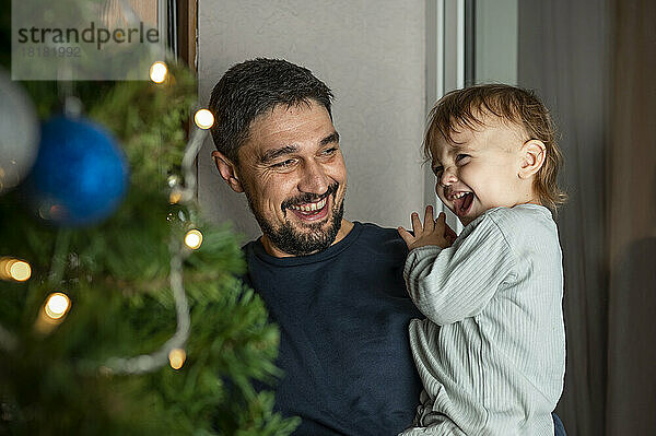 Glücklicher Vater trägt süßen Jungen vor dem Weihnachtsbaum zu Hause