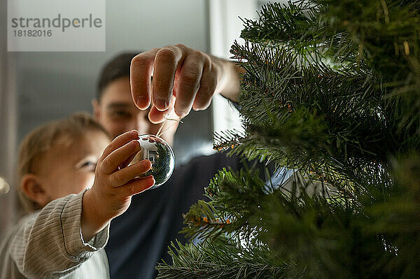 Junge mit Vater schmückt zu Hause den Weihnachtsbaum