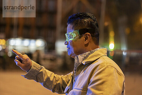 Reifer Mann mit Smart-Brille gestikuliert nachts auf dem Fußweg