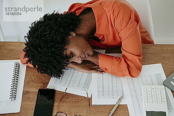 Müde junge Geschäftsfrau lehnt im Heimbüro am Schreibtisch