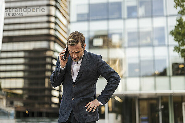 Angespannter Geschäftsmann  der vor dem Bürogebäude mit dem Smartphone spricht