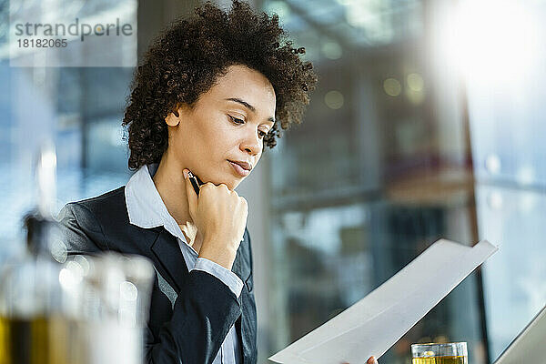 Geschäftsfrau mit Hand am Kinn liest Dokument im Büro
