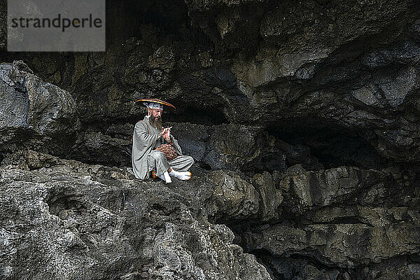 Mönch trägt Hut und praktiziert Meditation auf einem Felsen