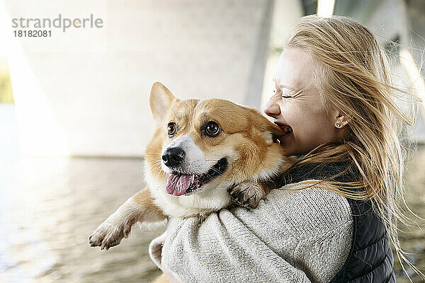 Blonde Frau lacht und hält einen süßen Hund in der Hand  der die Zunge herausstreckt