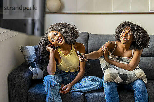 Lächelndes lesbisches Paar  das auf dem Sofa im Wohnzimmer fernsieht
