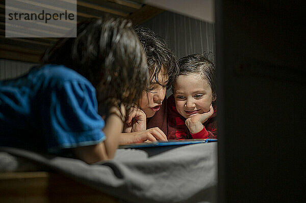 Boy reading book to brothers on bed at home