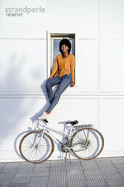 Lächelnde Frau mit Fahrrad sitzt auf der Fensterbank