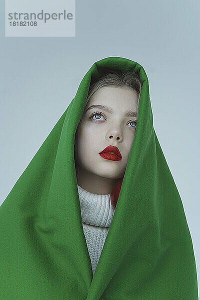 Thoughtful girl wrapped in green velvet cloth against white background