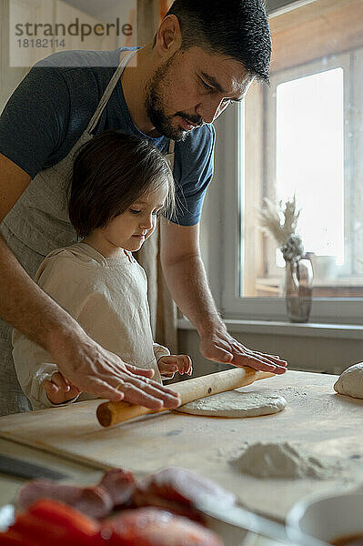 Junge mit Vater rollt Pizzateig in der Küche