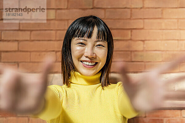 Happy young woman with bangs hair standing in front of wall