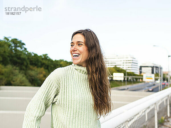 Cheerful woman wearing turtleneck sweater standing by railing