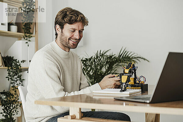 Lächelnder Ingenieur  der im Büro an einem Robotermodellarm arbeitet