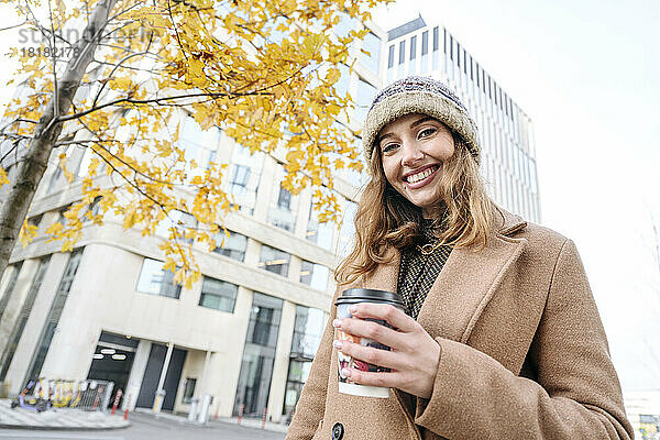 Glückliche Frau mit Kaffeetasse  die vor dem Gebäude steht