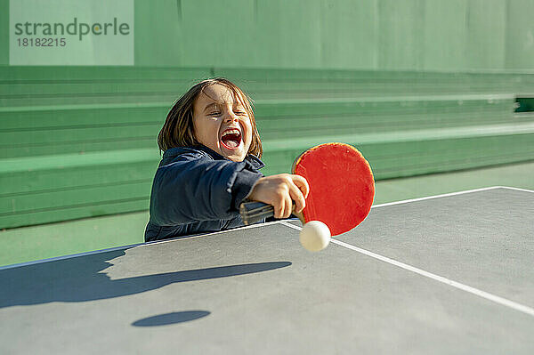 Fröhlicher Junge  der an einem sonnigen Tag Tischtennis spielt
