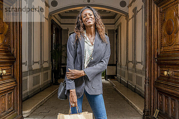 Lächelnde Frau mit Einkaufstüten steht vor der Tür