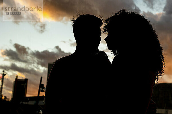 Silhouette eines jungen Paares unter bewölktem Himmel bei Sonnenuntergang