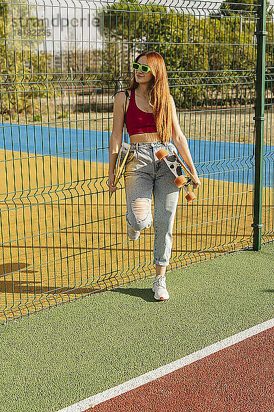 Junge Frau mit Sonnenbrille steht am Sportplatz