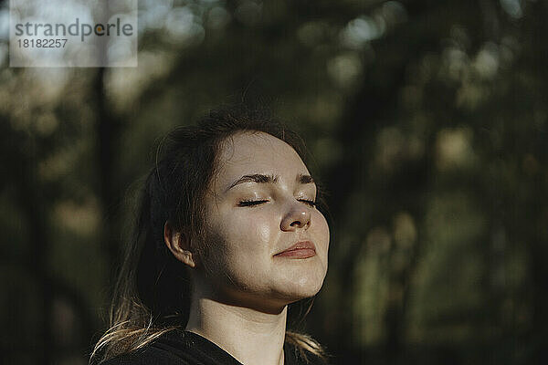 Lächelnde Frau mit geschlossenen Augen genießt die frische Luft in der Natur im Park