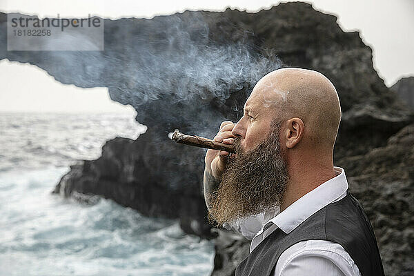 Reifer Mann raucht Zigarre vor Felsen