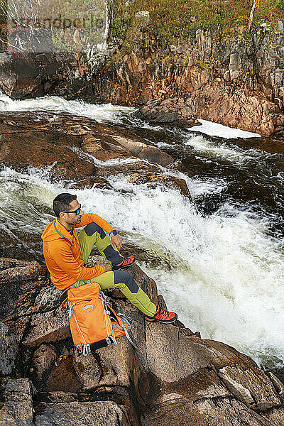 Mann mit Rucksack genießt es  auf einem Felsen zu sitzen