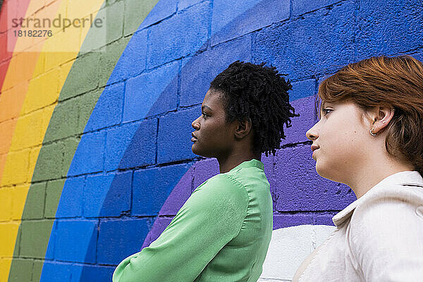 Nachdenkliche Frau mit Freundin an regenbogenfarbener Wand